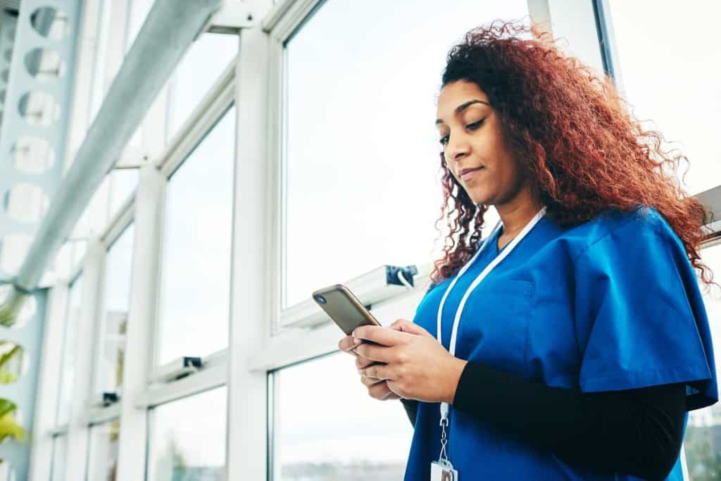 A female clinical using her smartphone wearing blue scrubs